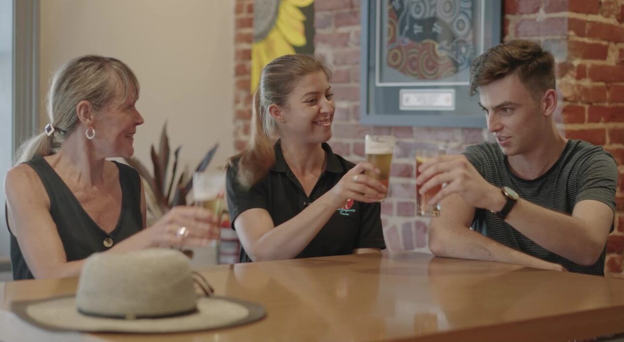 Photo of Katina and two travellers of Flamboyance Tours toasting their schooners at a pub in Port Adelaide